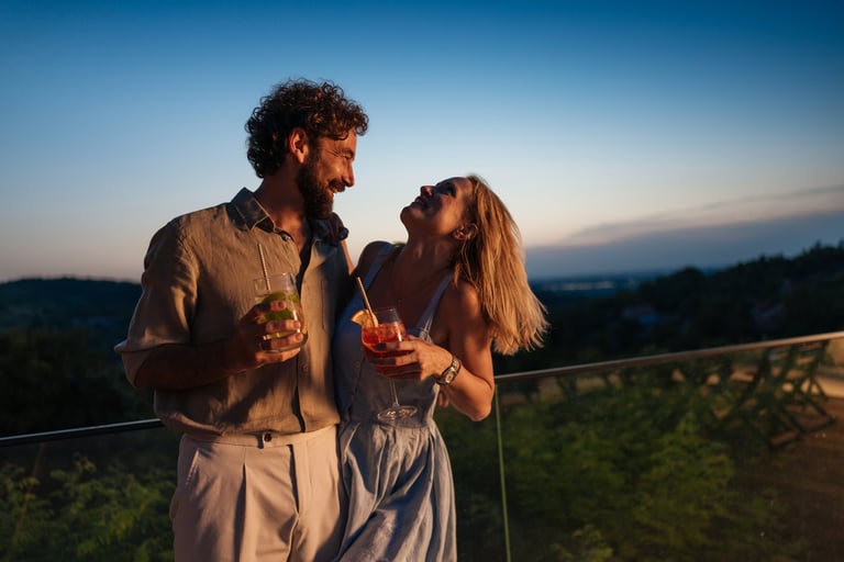 Romantic couple embracing and holding cocktails enjoying beautiful sunset view