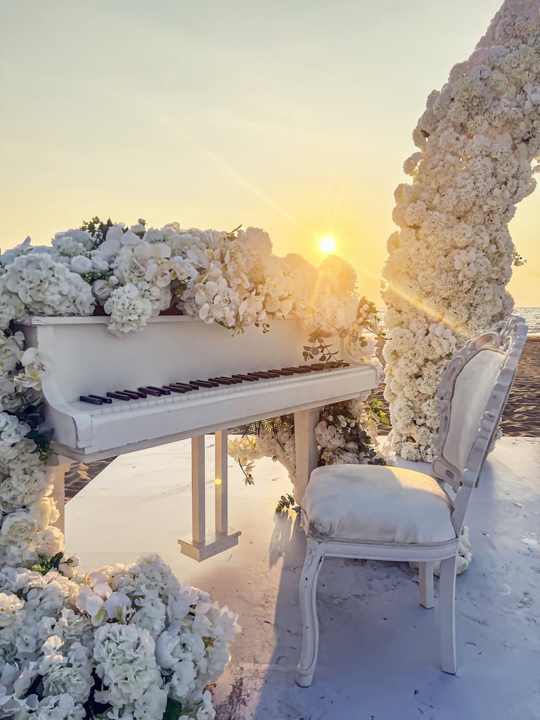 Romantic beach wedding ceremony with white piano and floral decorations at sunset.